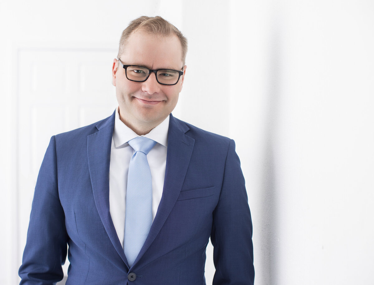 Janel Lee Photography captures the essence of professional charm in this bright and airy Cincinnati studio portrait of Matt Kahn. Matt's headshot is a perfect blend of personal branding and professional elegance, featuring him in a sharp blue suit with a light blue tie, complementing his light-colored shirt. His glasses add a touch of intellectual sophistication to his friendly smile, making this image ideal for corporate profiles and business networking.