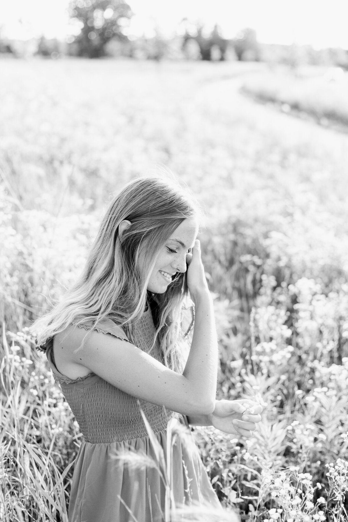 girl sitting in a field playing with her hair and looking at flowers