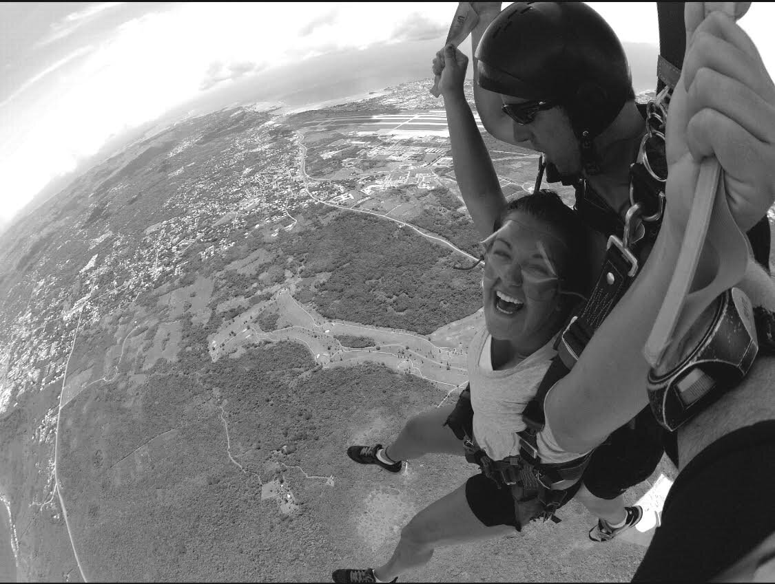 Nicole Harkness smiling while jumping out of a plane with a parachute.