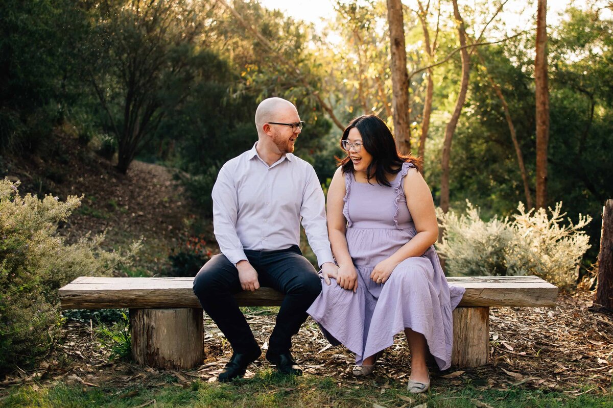 Man and pregnant woman sitting on bench, laughing. Taken during Melbourne maternity photoshoot. 