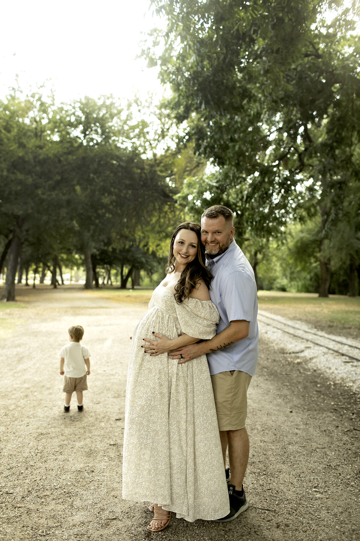 A joyful maternity moment at Trinity Park, with mom and dad laughing as big brother runs ahead, enjoying the outdoors, captured by Chunky Monkey Photography.