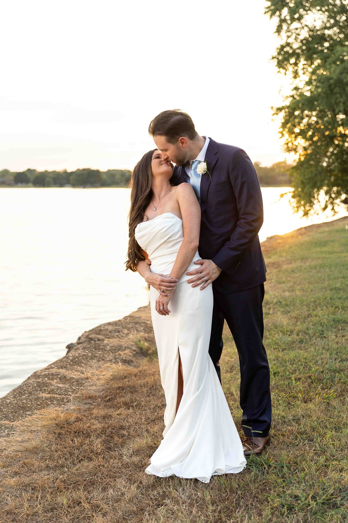 Bride and groom embracing and kissing in front of sunset