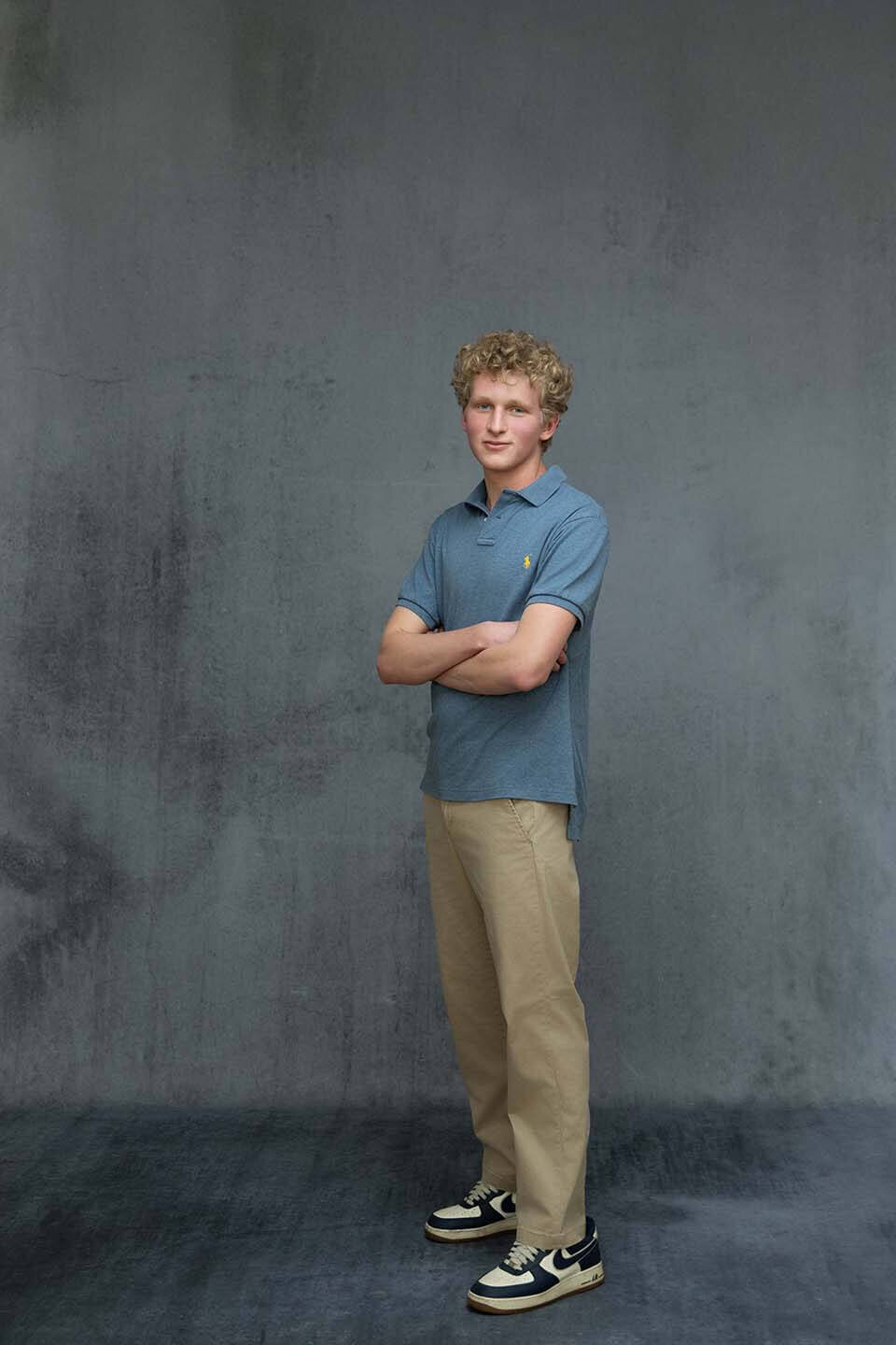 senior-guy-standing-in-studio-against-gray