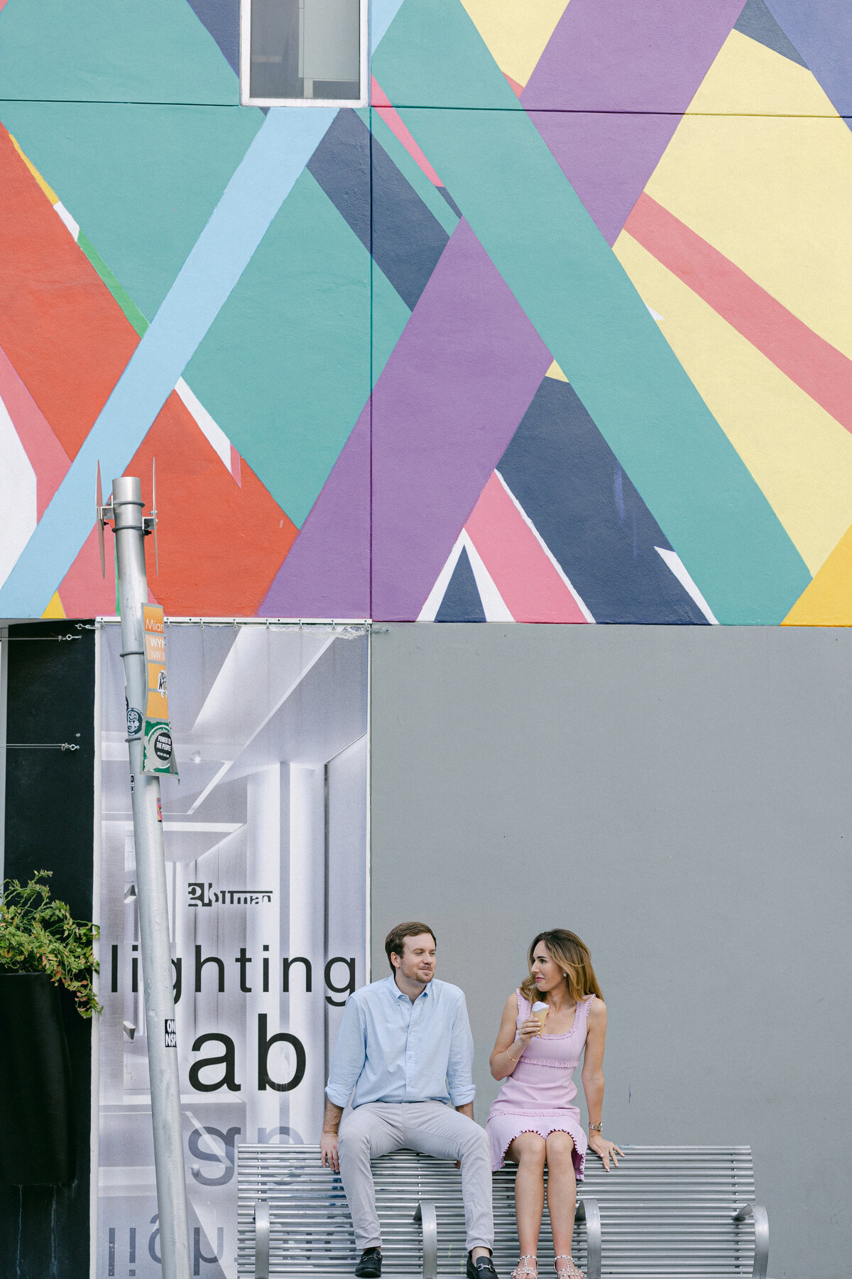 Couple sitting on a bench in front of a vibrant, colorful mural in Miami, captured by Rodrigo Varela Photography.