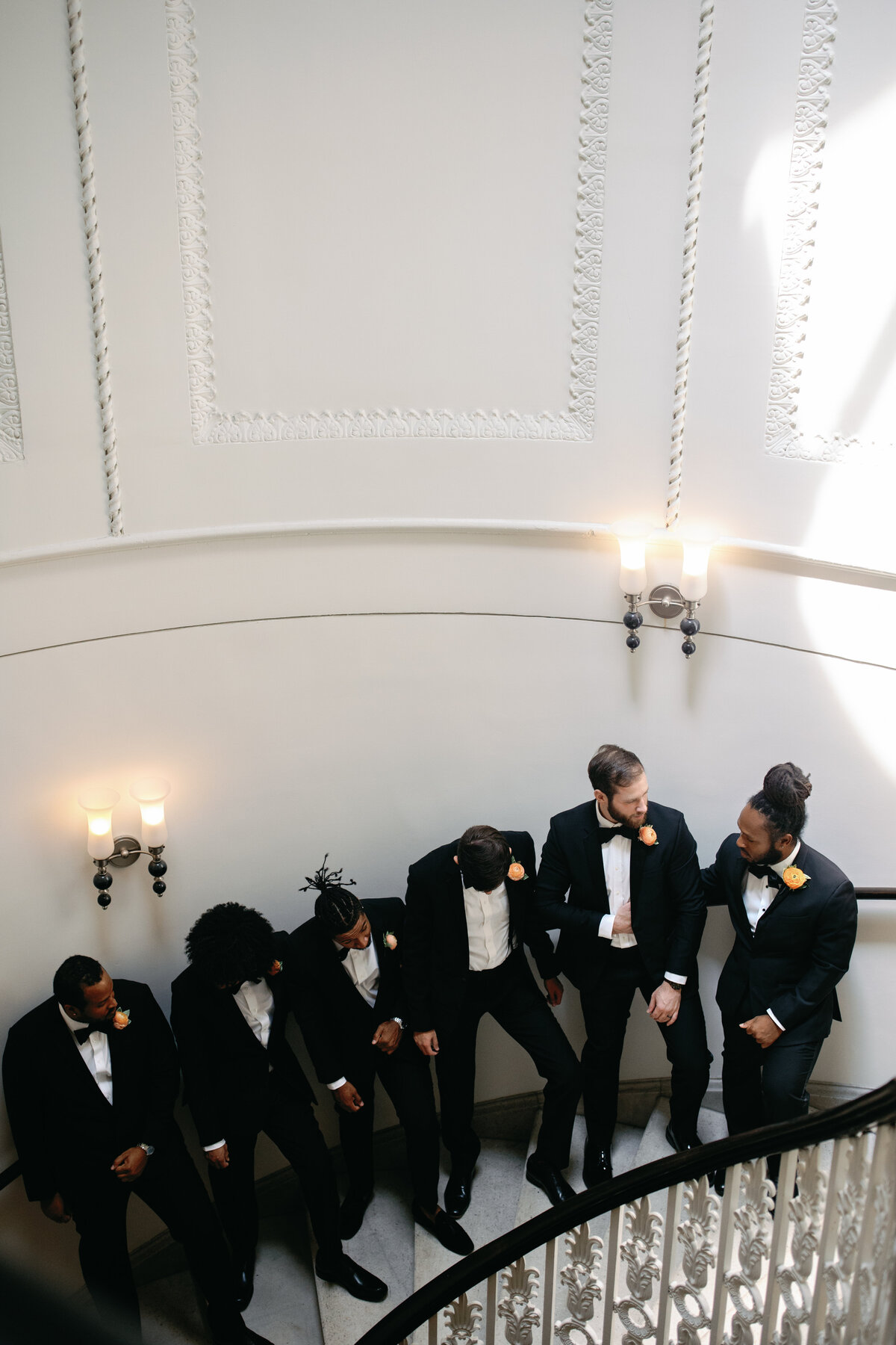Groomsmen in black tuxedos posing on spiral staircase inside Hotel Monaco DC.