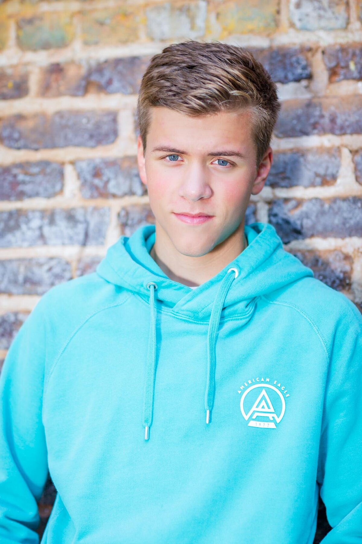 Handsome senior leaning  against a brick wall in Senoia wearing a blue sweatshirt.