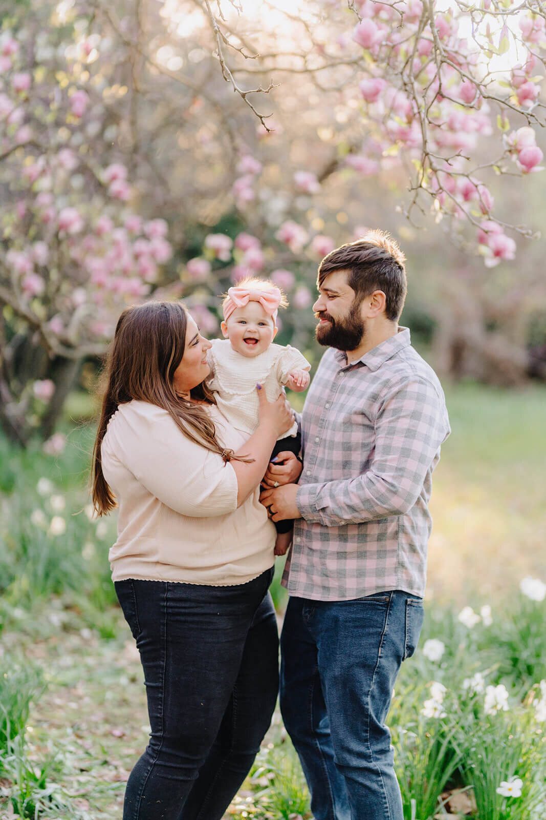 couple holding a baby standing in front of cherry blossom tree