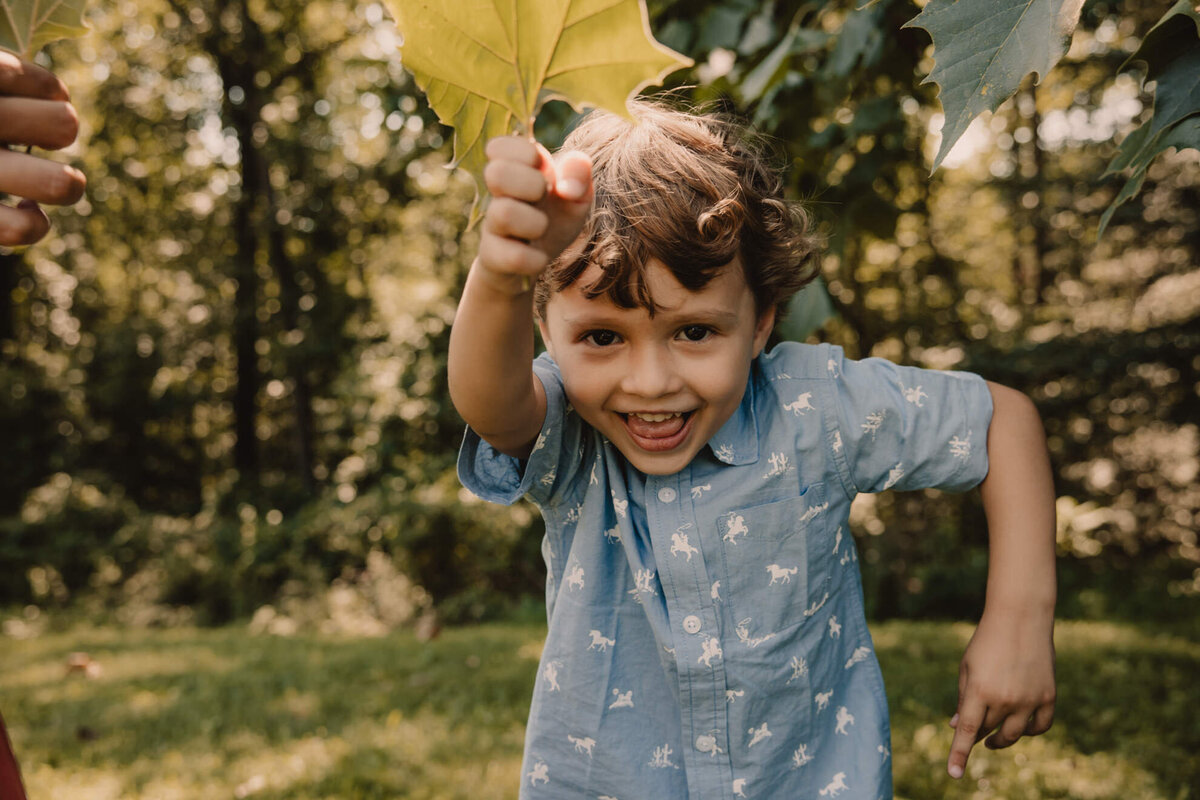 A child smiling and holding up a leaf 