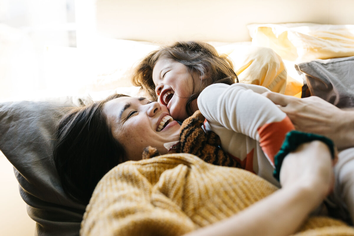Mother and daughter laughing and cuddling in bed.