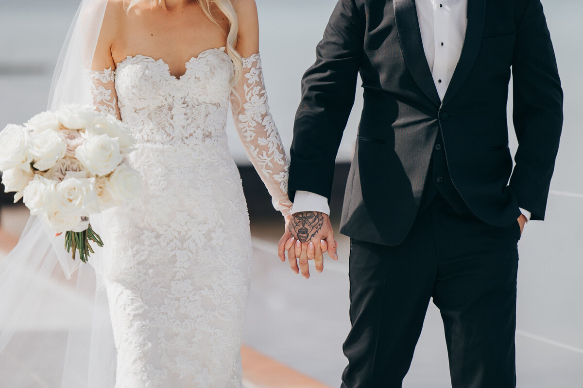 Glamorous bride and groom holding hands in sunny wedding portraits