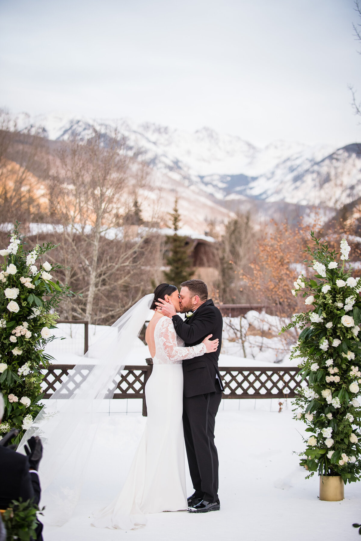 A groom grabs his bride's face and kisses her at the end of their ceremony with snowy Colorado mountains in the background.