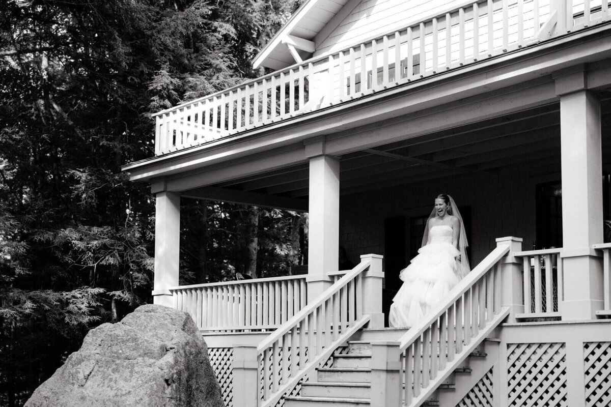 Black and white photo of the bride standing on top of the staircase of a porch at The Ausable Club, New York.