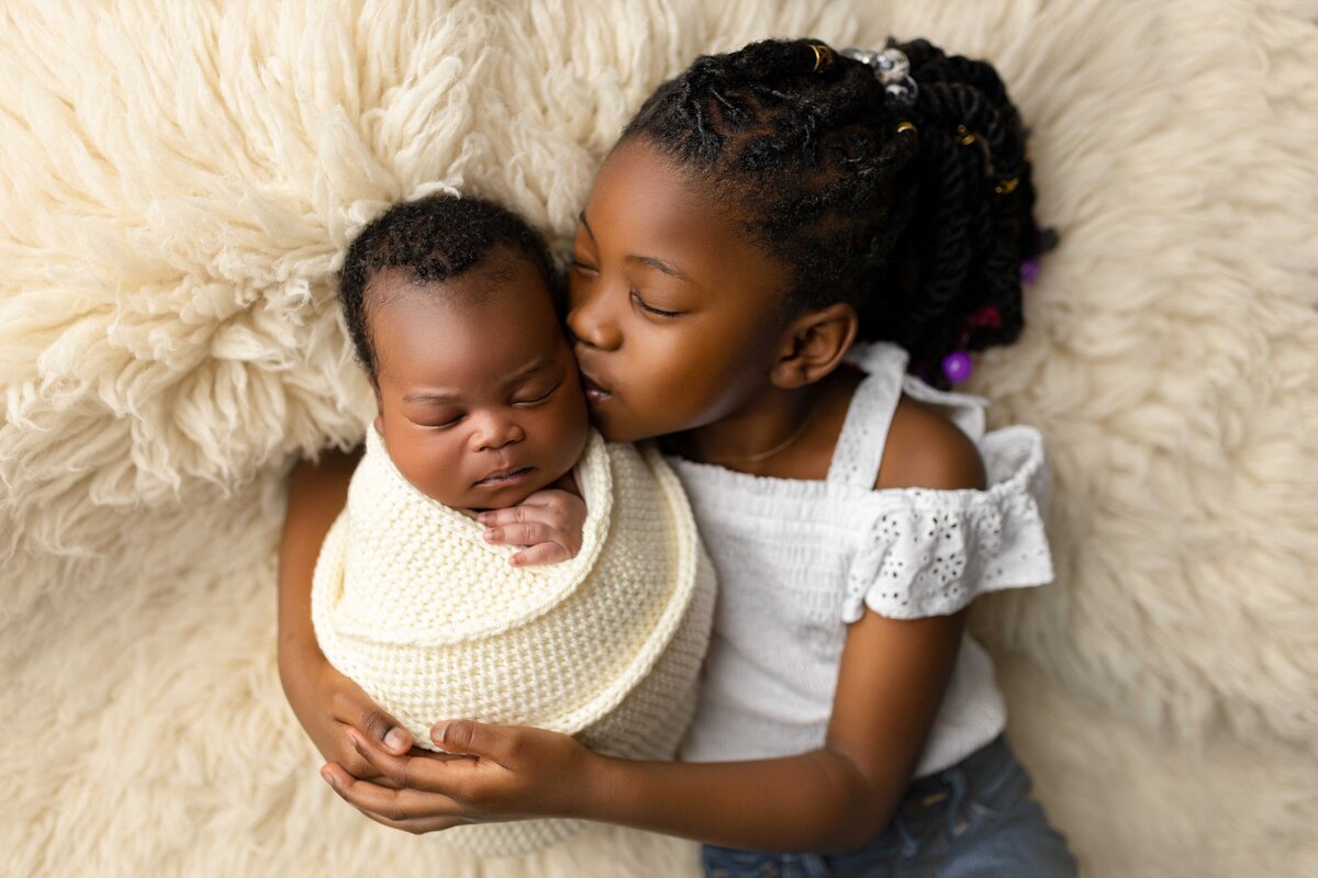 Big sister kissing her sleeping newborn brothers cheek during  Charleston newborn photography session