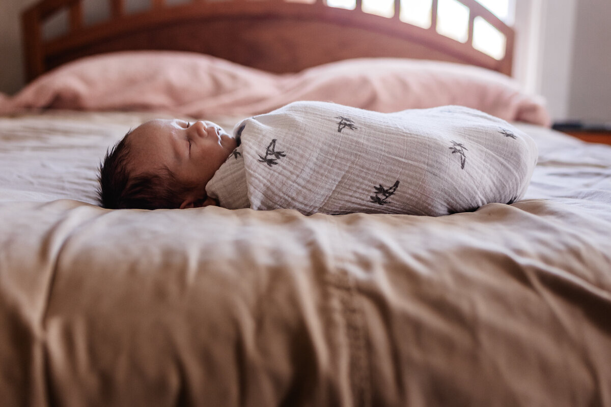 Swaddled baby on bed at in-home newborn photography session in Concord NH by Lisa Smith Photography