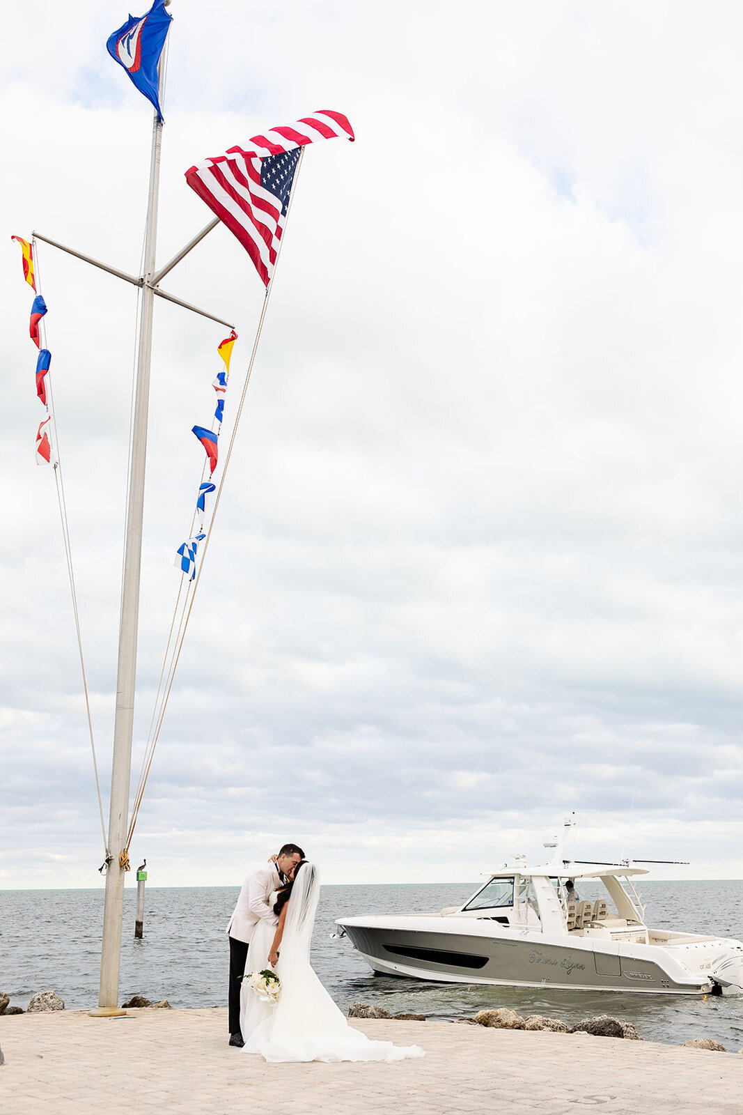 Ashley and Cameron share their first kiss as a married couple, standing by the sea at Ocean Reef in Key Largo, with a luxury boat in the background.