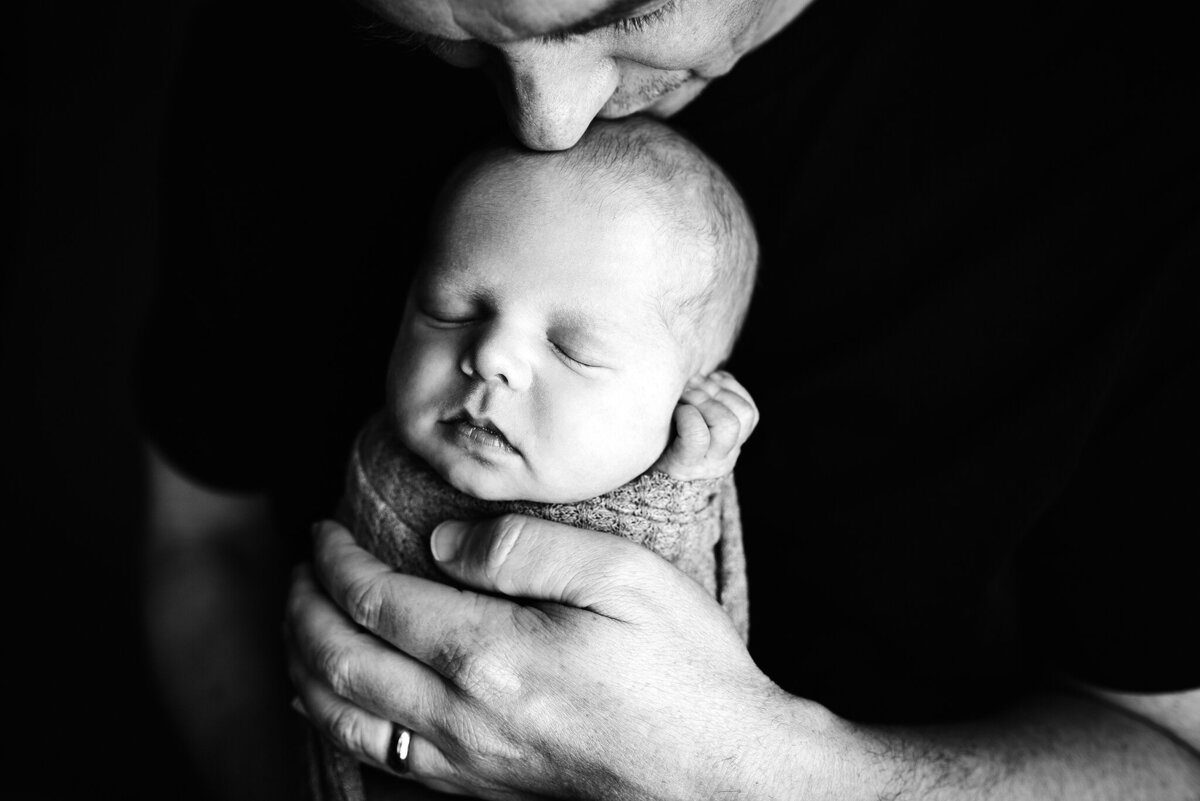 Black and white studio portrait of dad kissing top of baby's head in Jacksonville, Florida.