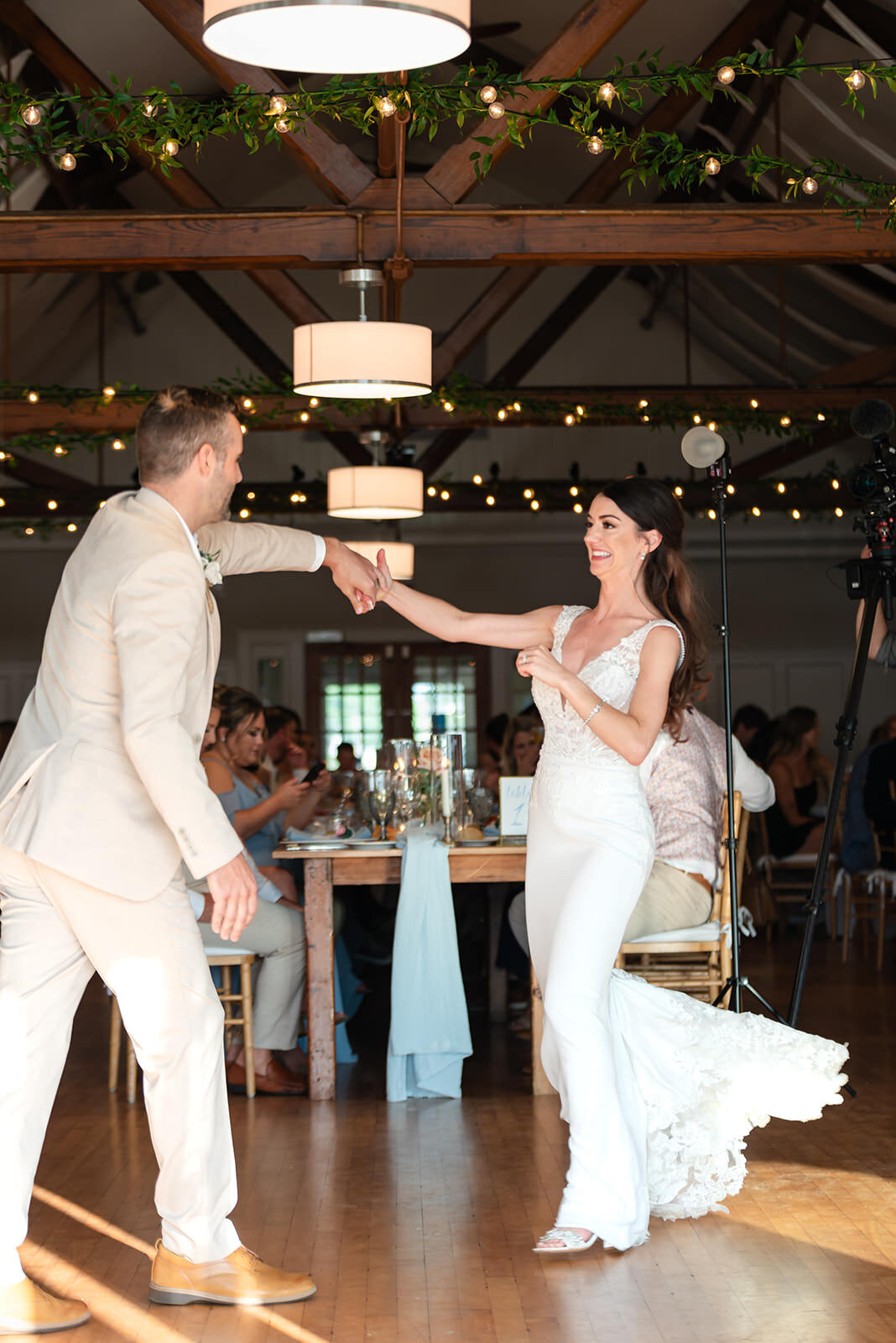 The bride playfully leads the groom onto the dance floor, with the wedding party watching and smiling.