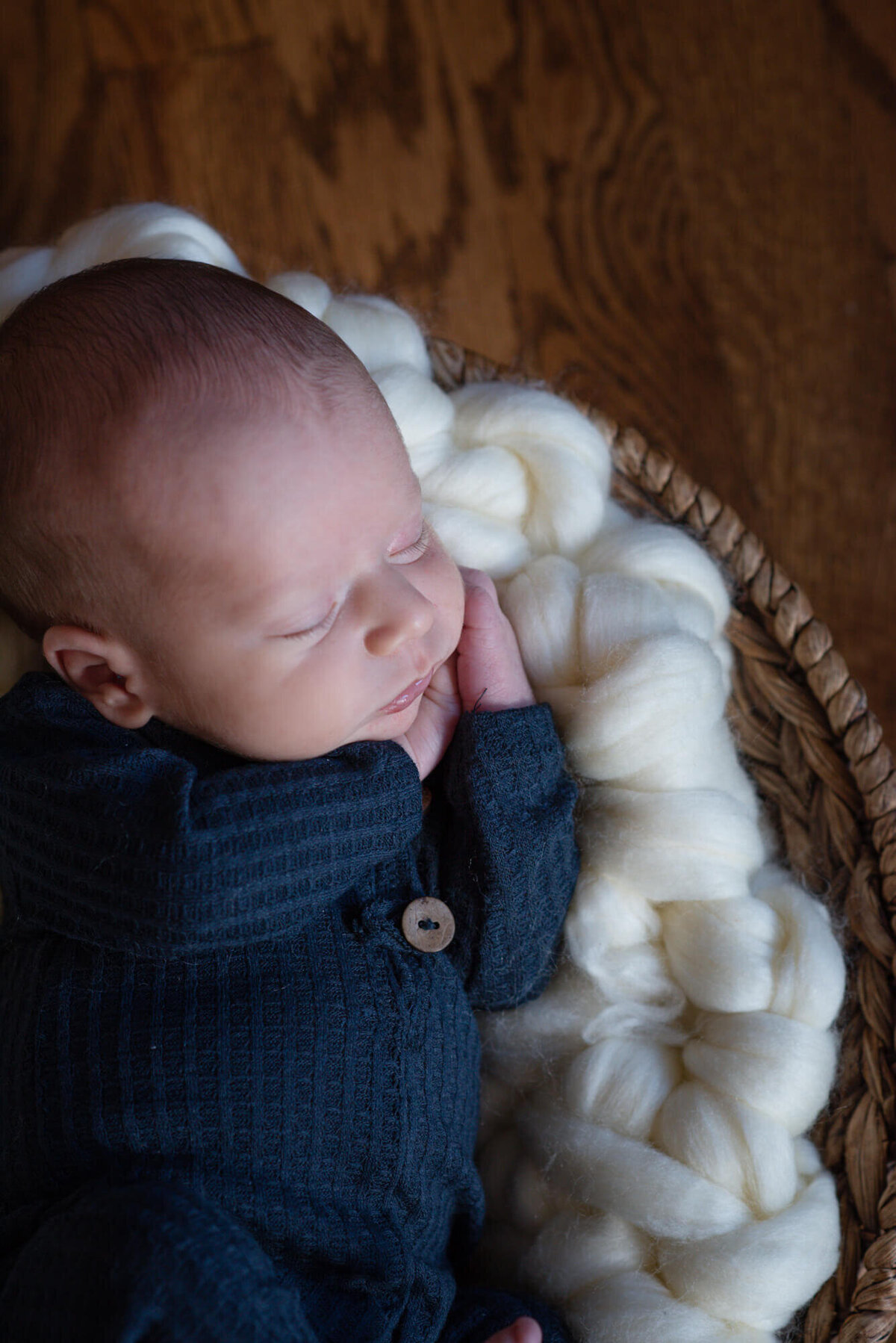 A newborn baby sleeps on its hands while in a woven basket as posed by a Denver Newborn Photographer