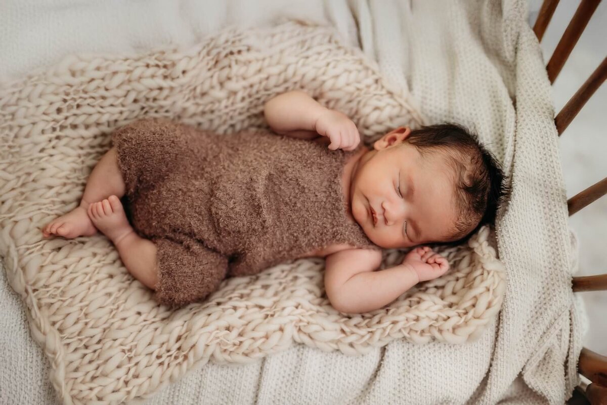 newborn baby boy in a fuzzy romper on a knit blanket for his studio photoshoot