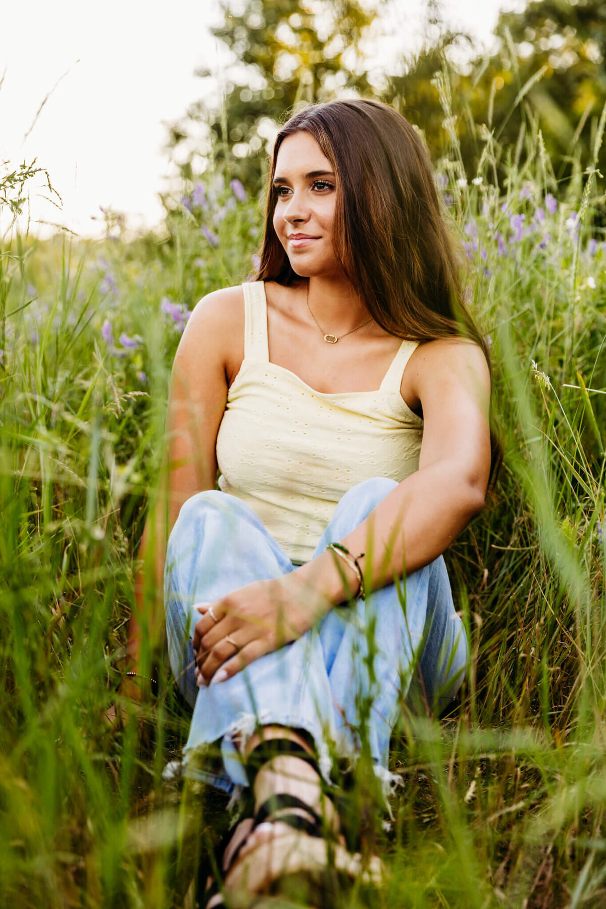 pretty high school girl looking off to the side as she sits in the middle of a field for her senior photography session