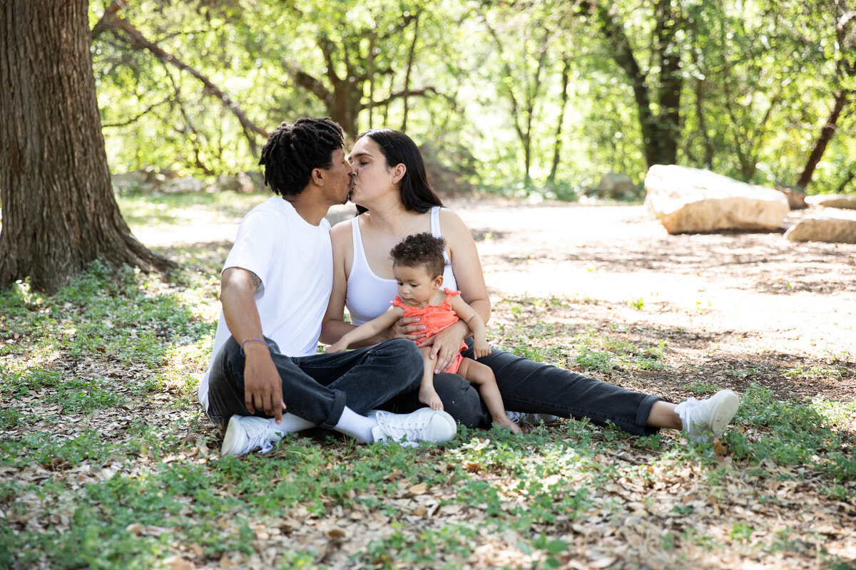 Austin wedding photographer captures beautiful moments as a family sits on the grass, sharing kisses with each other.