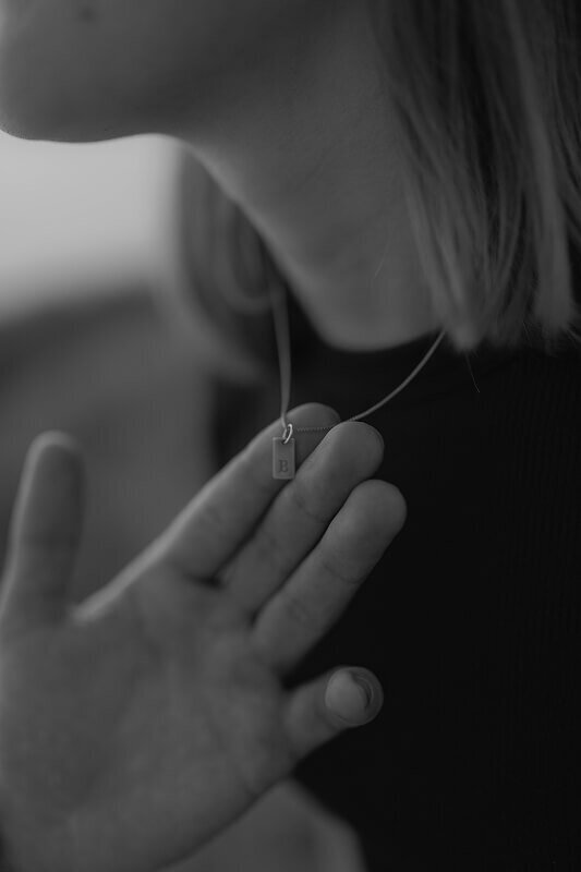 Black and white close up photo of a man showing off his girlfriend's necklace.