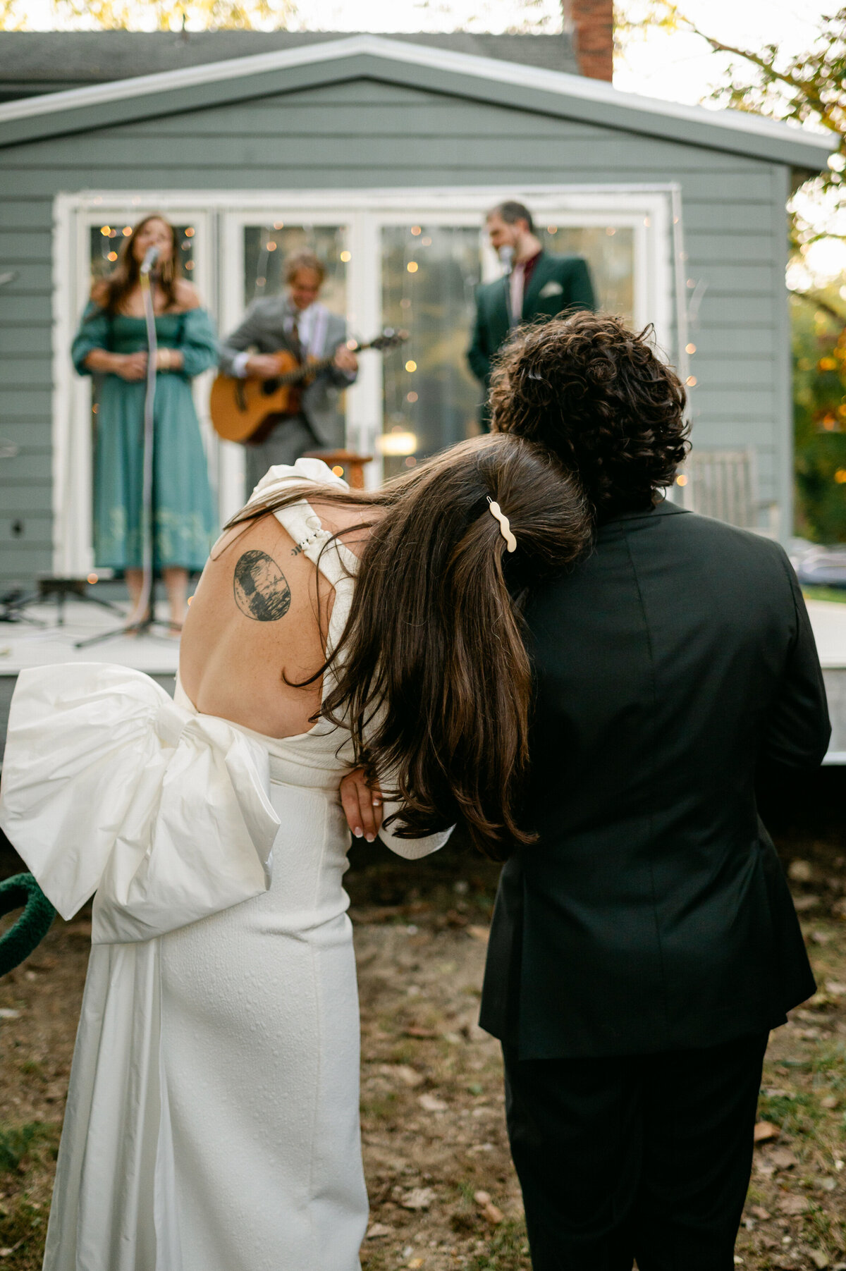Bride leaning head on groom's shoulder while they watch the band