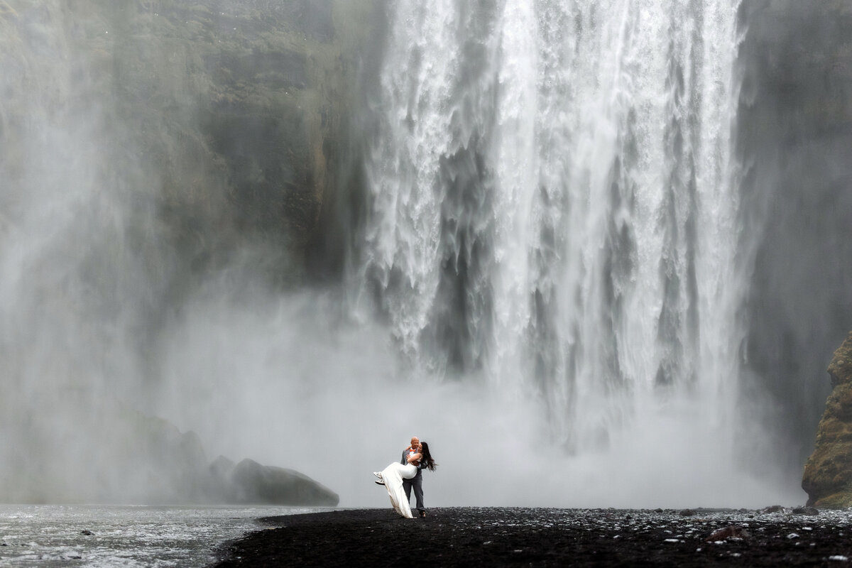 Intimate elopement photo of a couple kissing beneath the majestic waterfalls of Iceland, showcasing their love amidst nature's grandeur