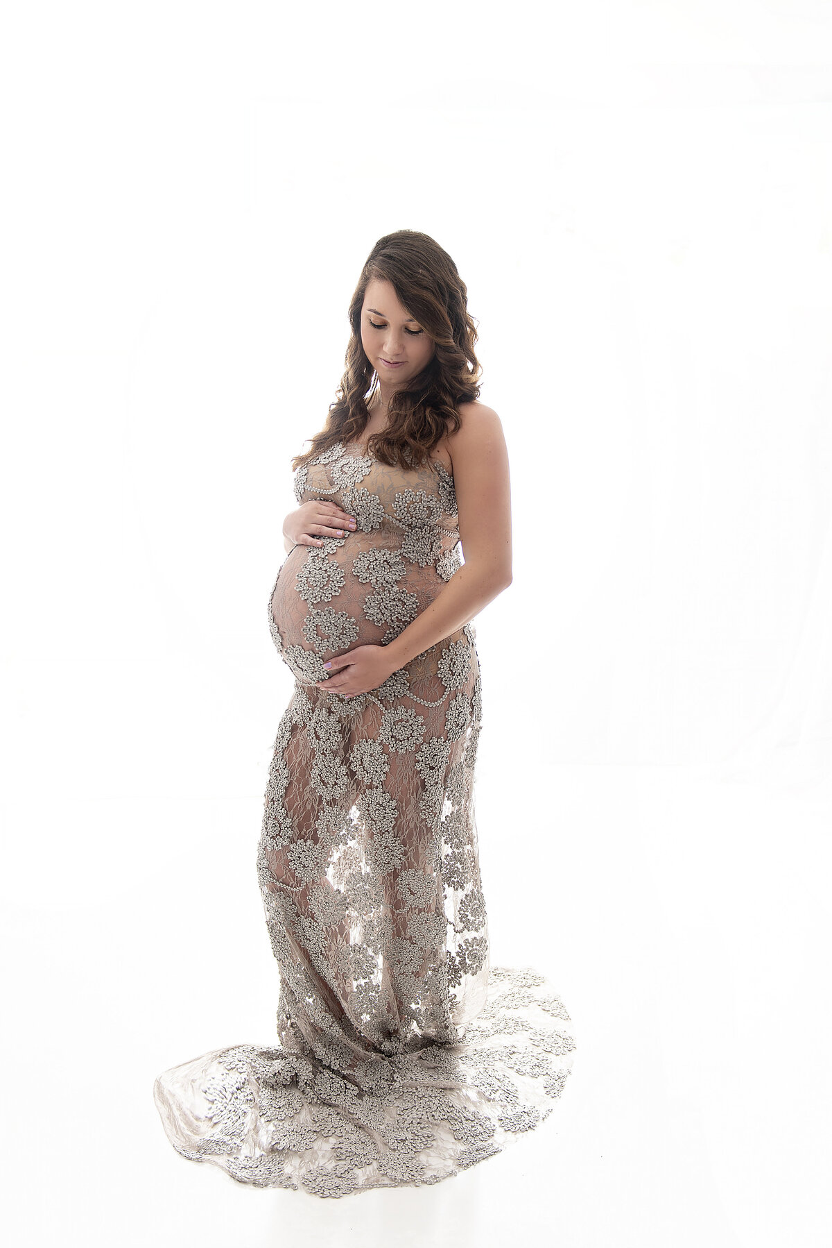 A mother to be smiles down at her bump while wearing a gray lace gown