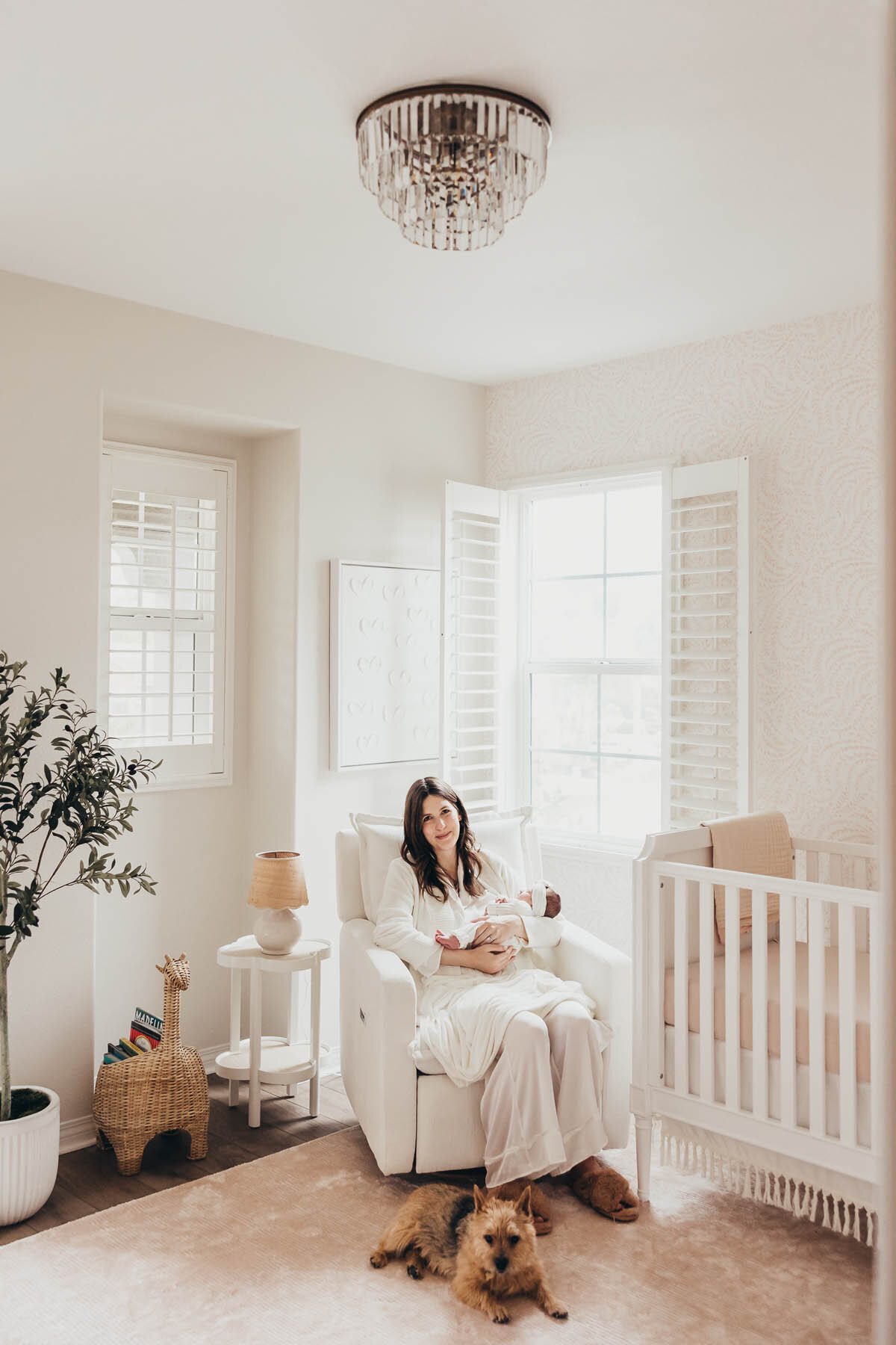 a new mother sits in her baby's nursery holding her baby with her brown dog at her feet.