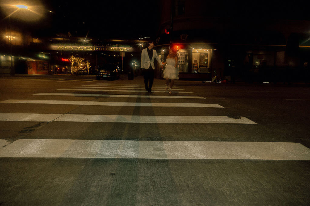 A newlywed couple walking across a crosswalk.