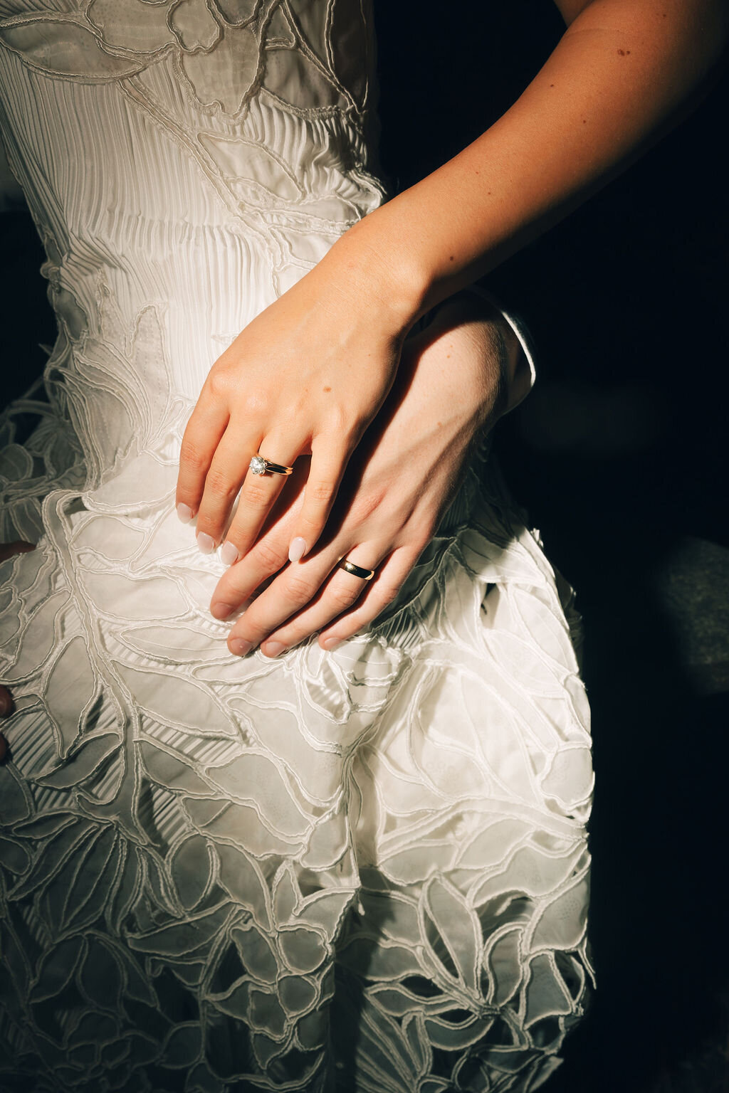 Bride and groom standing at an ivy covered alter laughing as groom puts wedding band on bride's finger