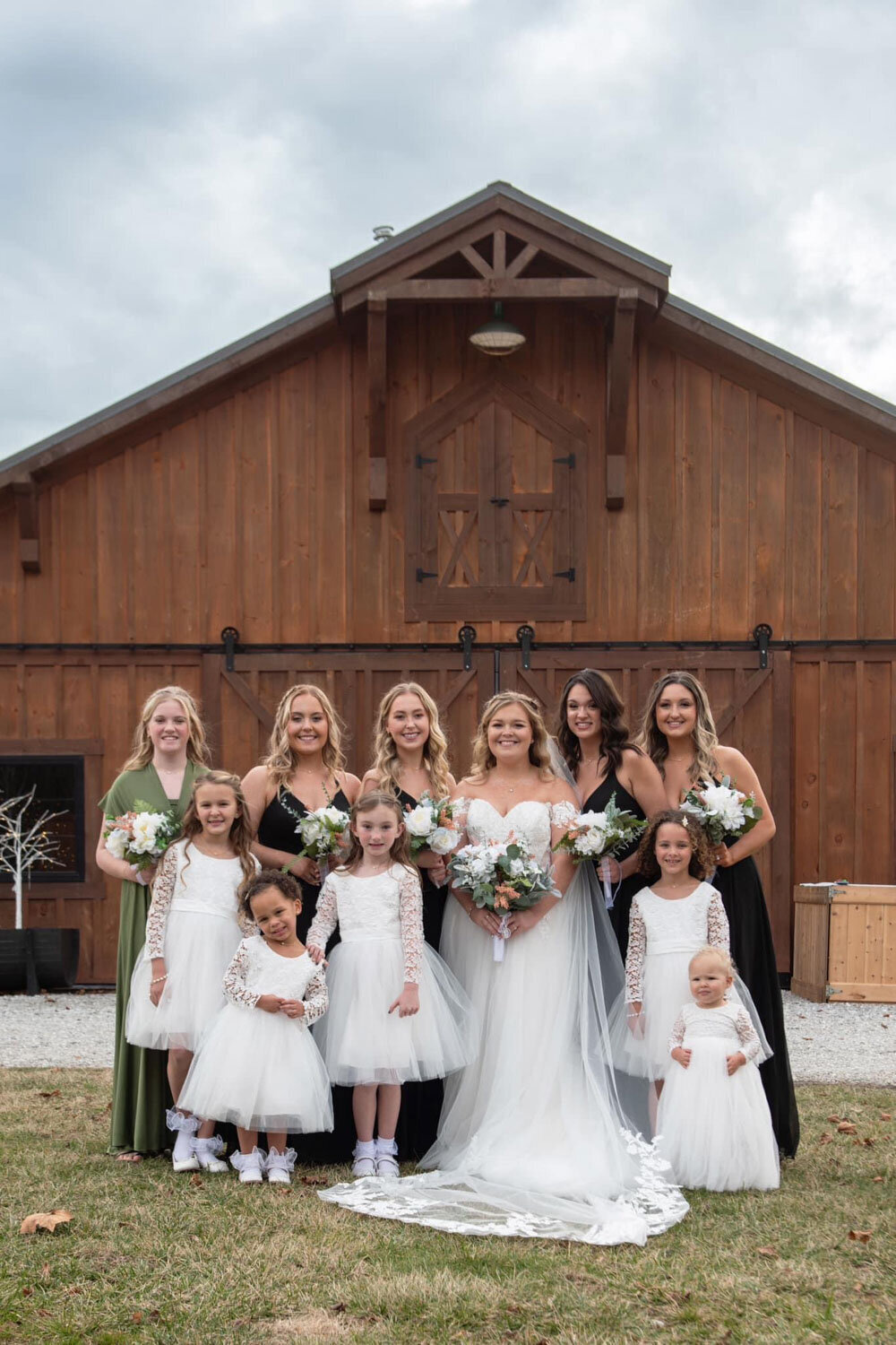 Bride with bridesmaids and flower girls in front of a barn