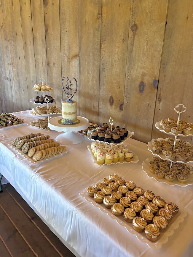 A table is filled with white plates and stands full of mini pastries and cookies, with a small naked style cutting cake in the center. 