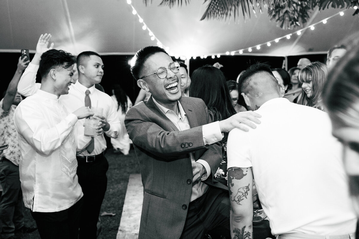 Candid black and white photo of guests dancing and laughing on the dancefloor, captured in a candid wedding photography style — by Kate Winters Photography.