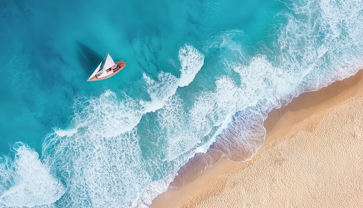 Overhead view of a yacht sailing close to the shoreline as waves roll in