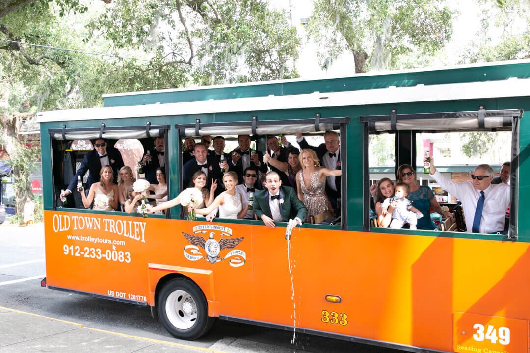 A large wedding party celebrates on the Old Town Trolley hanging out the windows