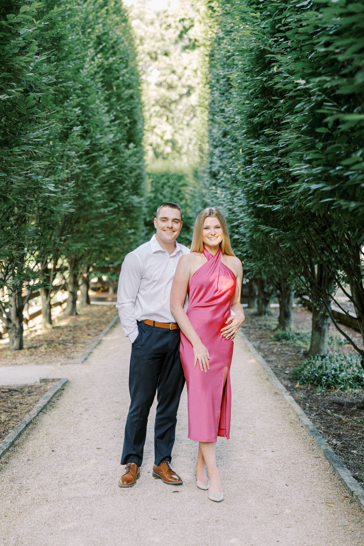 Engaged couple smiling on tree-lined path in Columbus park shot by Philadelphia photographer.