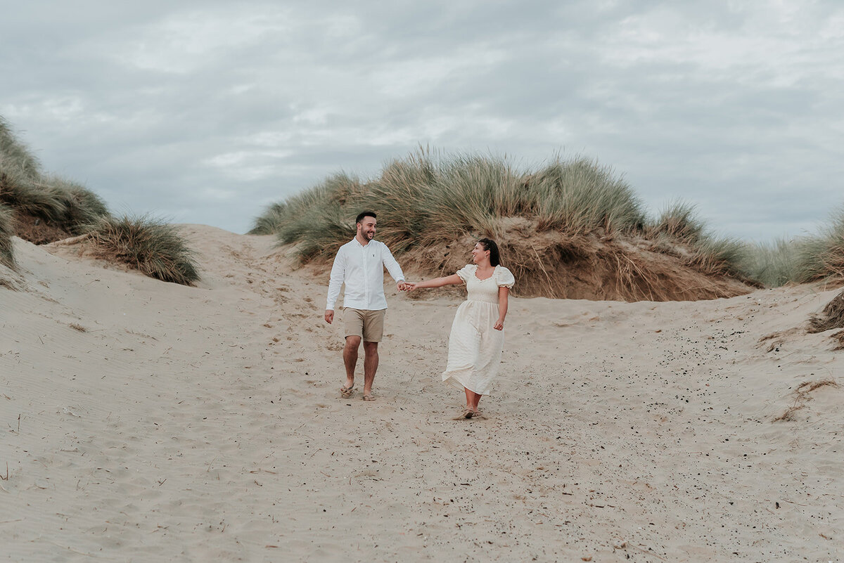 Couple hold hands and walk slowly through the sand at Camber Sands, Rye