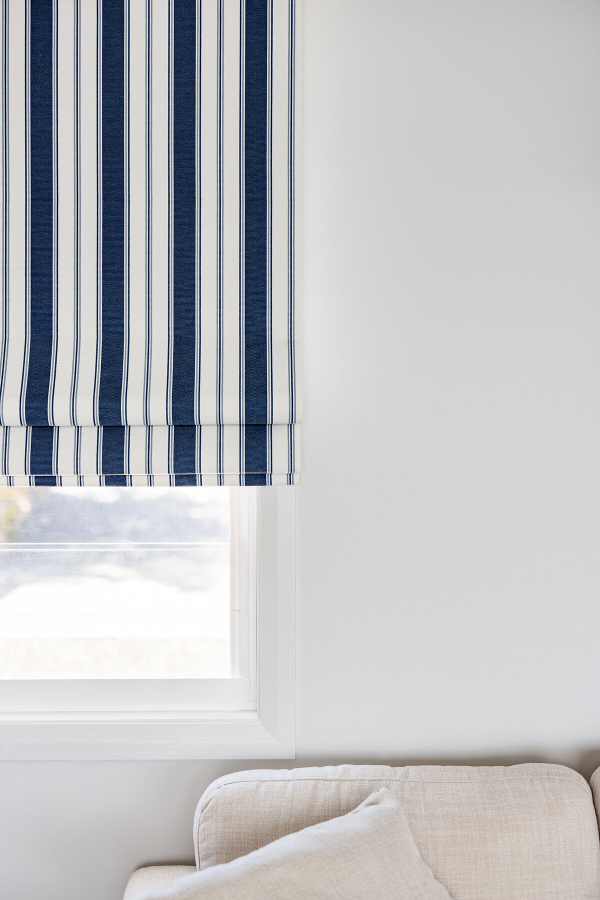 A blue and white striped curtain hangs above a window next to a beige couch with a white cushion, showcasing the elegance of custom interior design Newcastle.