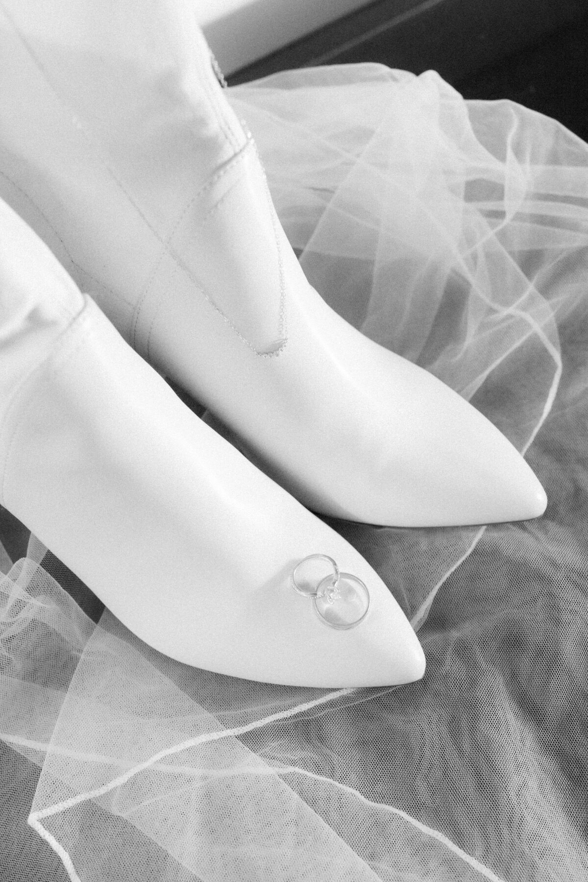 black and white detail image of bridal boots on a veil adorned with wedding bands and delicate necklace