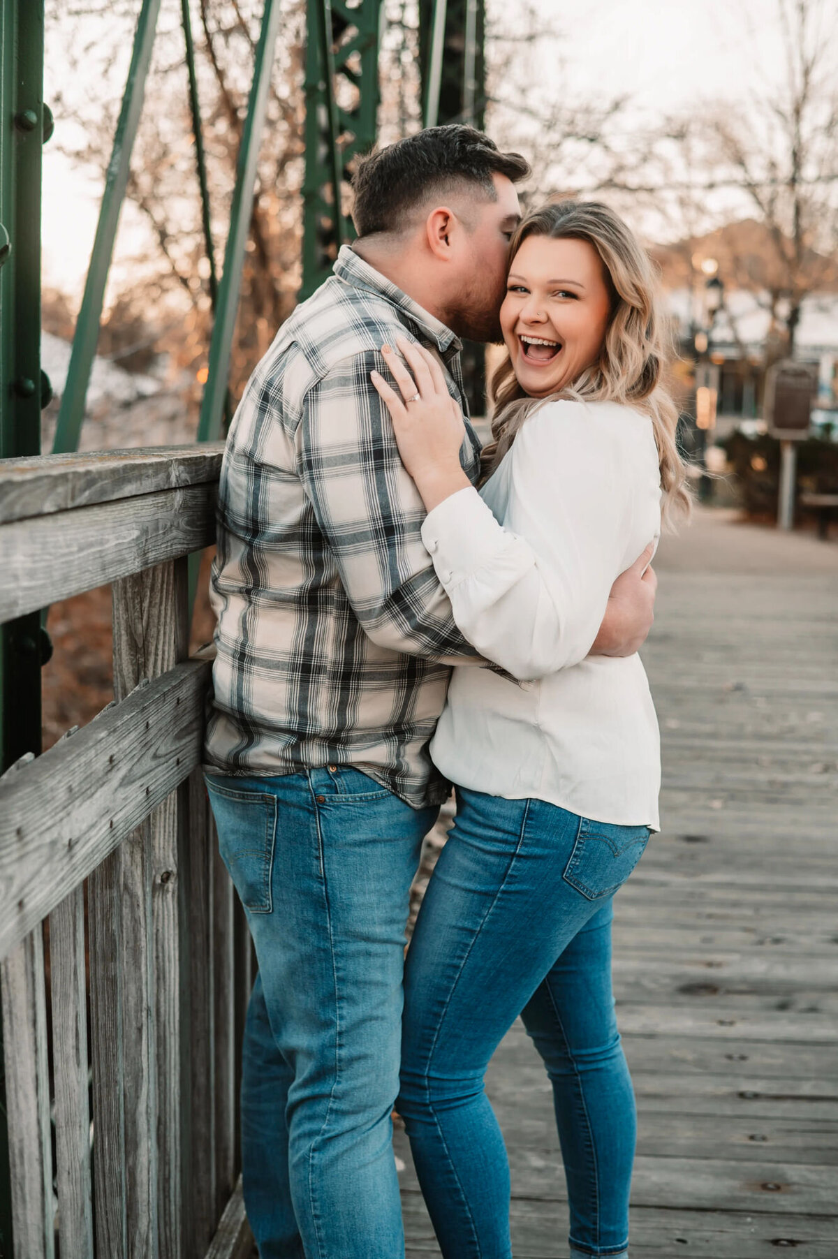 man whispers in womans ear as she laughs on a bridge in cedarburg