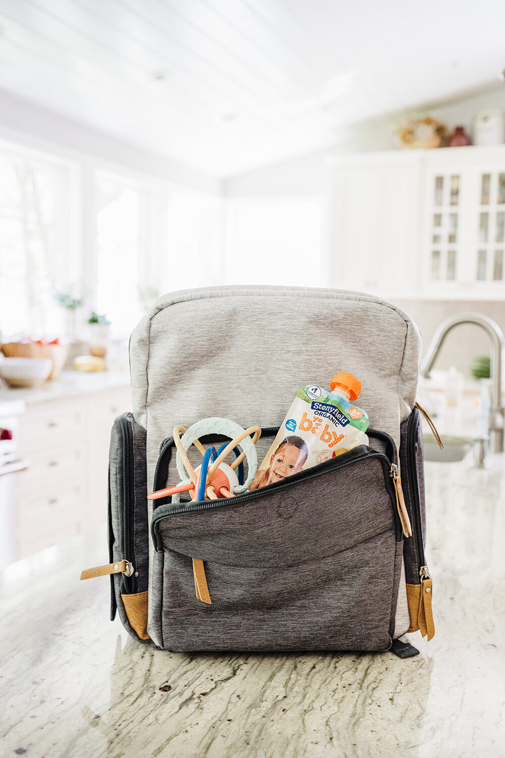 yogurt pouch and baby toy stuffed into front of backpack diaper bag