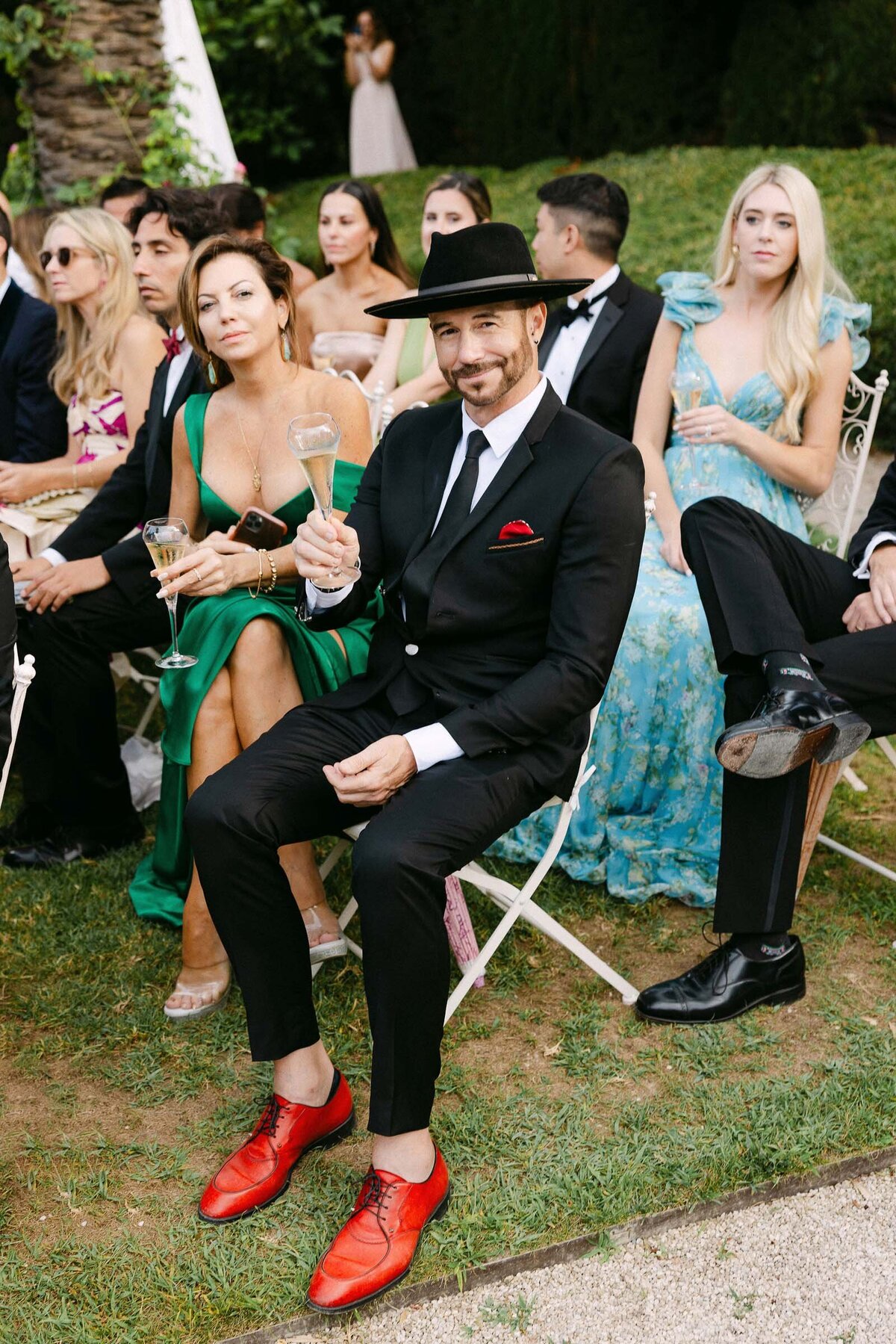 Stylish guest with black-tie attire, a hat and red shoes.