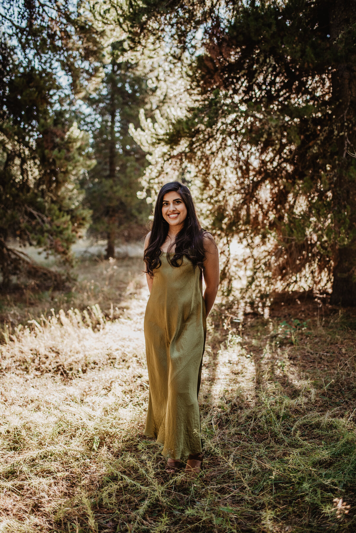 woman in an olive green velvet dress while standing in the forest in Jackson Hole for formal photos with photographers in jackson hole