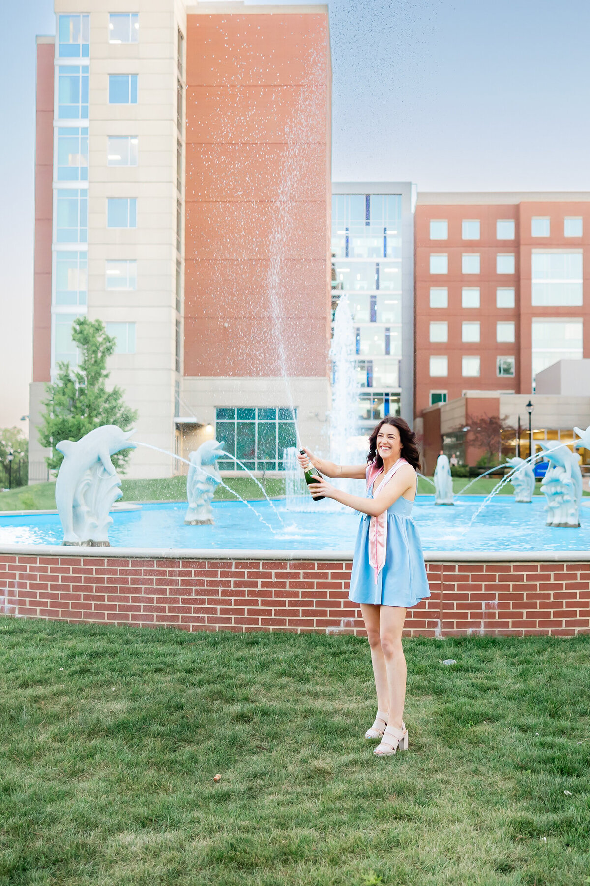 SLU senior girl with blue dress spraying a champagne bottle