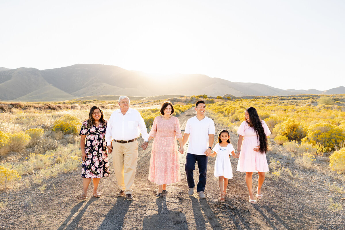 A family walking hand-in-hand along a rustic desert road, surrounded by golden wildflowers and mountains in Saratoga Springs Utah.