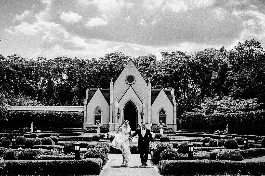 Black and white photo of bride and groom walking hand in hand away from a chapel after their NJ wedding ceremony.