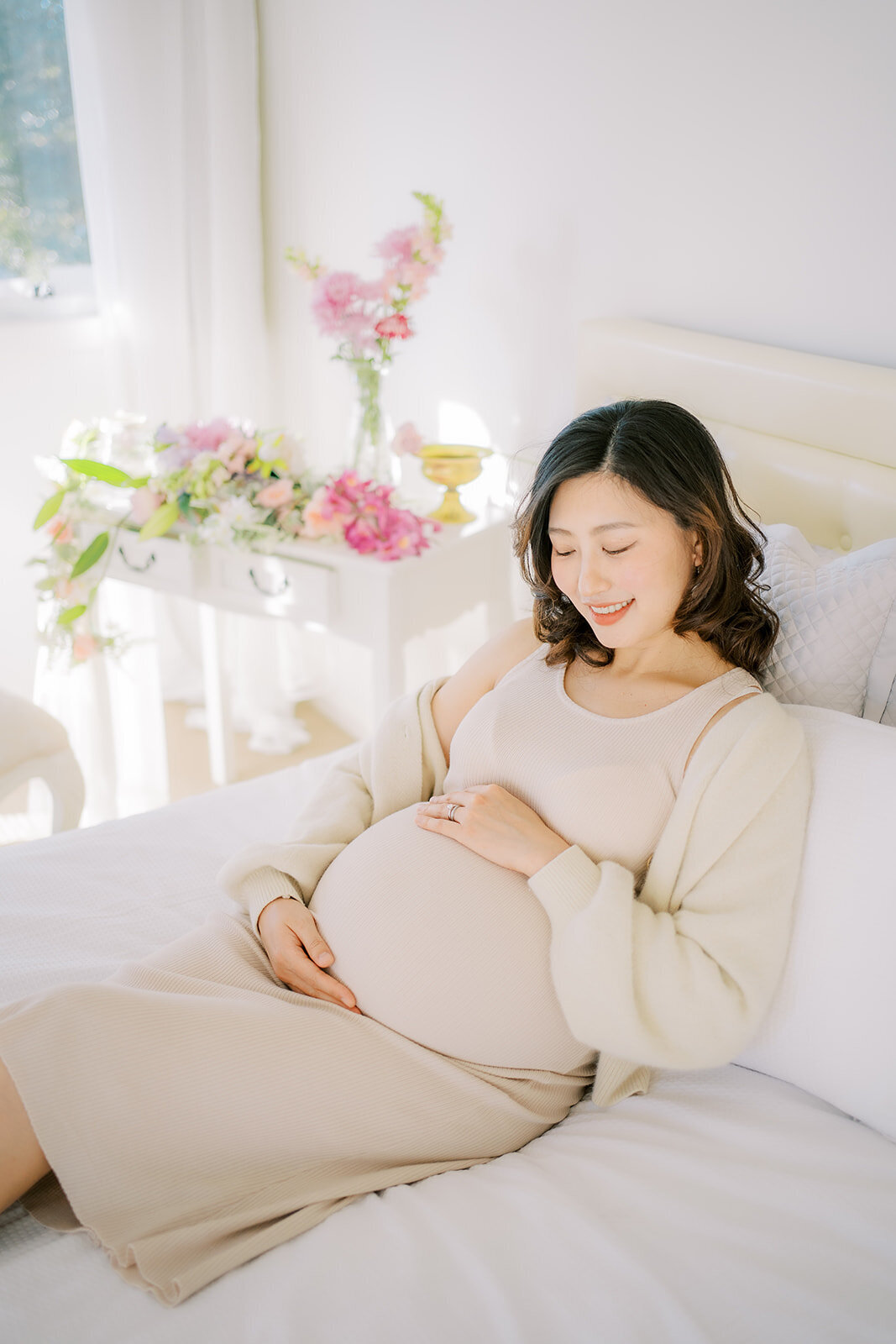 Pregnant woman holding bump dressed in beige ribbed knit dress having makeup done in Brisbane