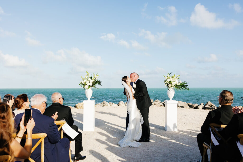 A breathtaking moment as the newlyweds share their first kiss, framed by ocean views and elegant floral arrangements. Captured by Claudia Amalia Photography, a Florida Keys wedding photographer specializing in destination wedding photography.